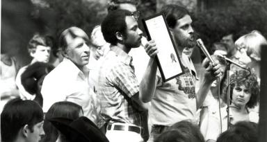 Deacon Maccubbin, John Wilson, and Frank Kameny stand at the stage to read the D.C. City Council's proclamation recognizing June 22, 1975 as Gay Pride Day. (Source: Rainbow History Project)