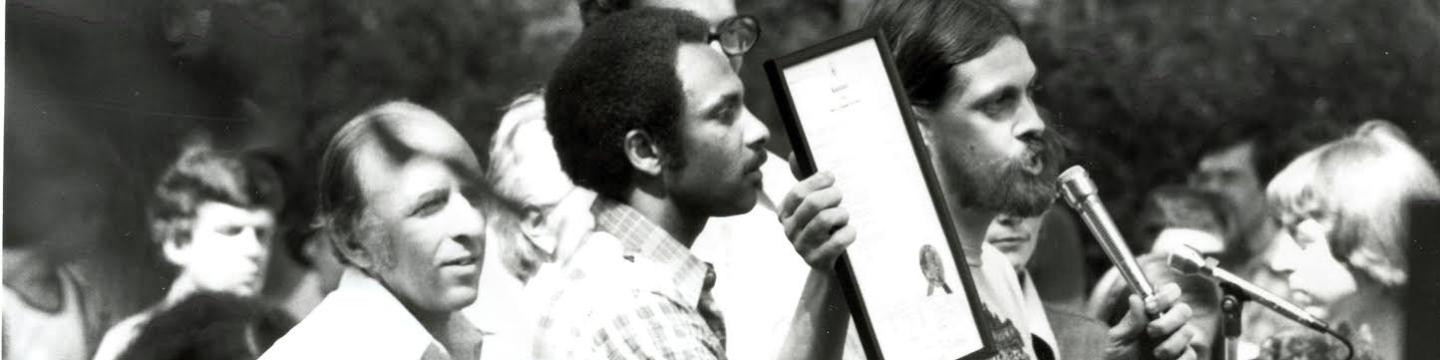Deacon Maccubbin, John Wilson, and Frank Kameny stand at the stage to read the D.C. City Council's proclamation recognizing June 22, 1975 as Gay Pride Day. (Source: Rainbow History Project)
